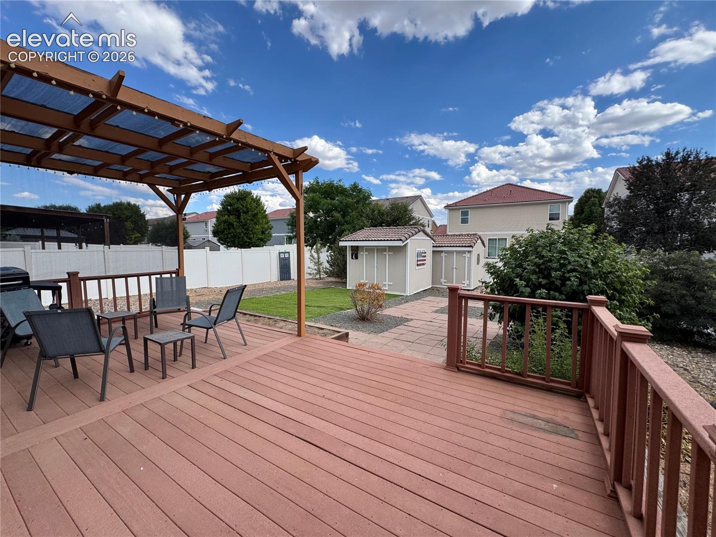 Expansive rear deck with a wood pergola featuring a translucent roof, extending to a paver patio