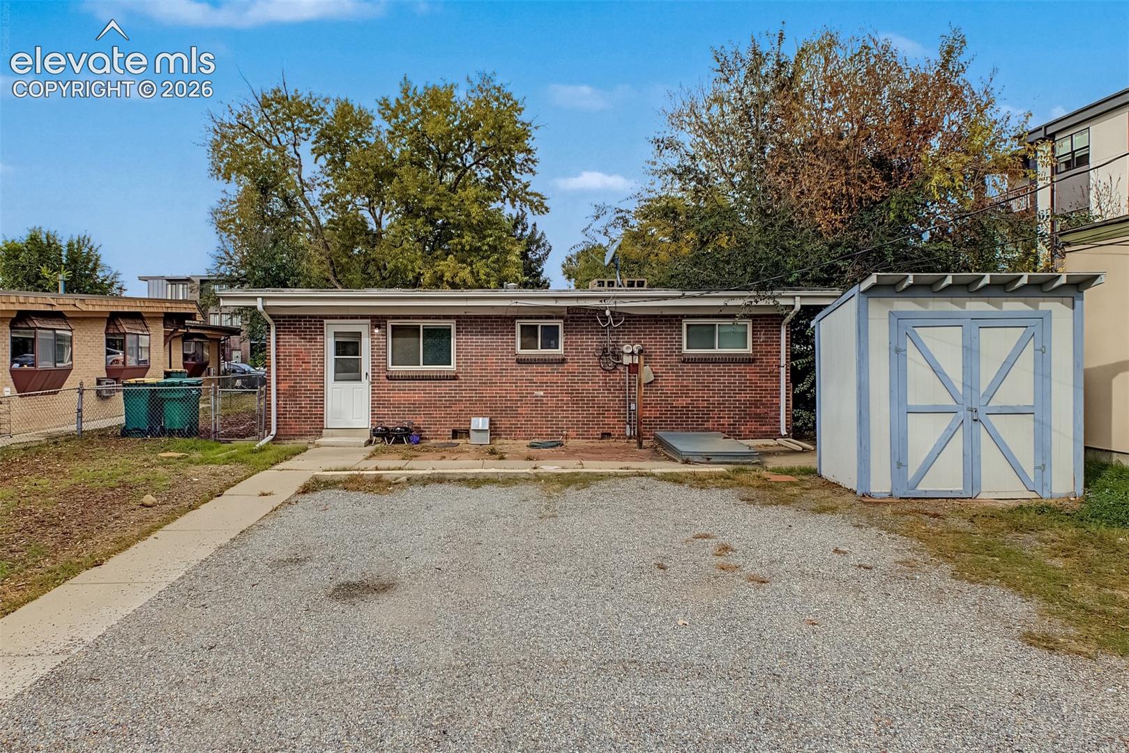 Brick exterior finish, gravel parking area, concrete walkway, and detached storage shed