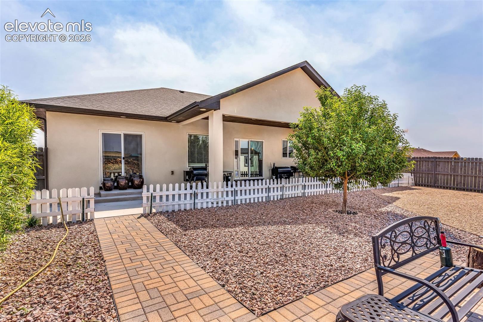 Expansive backyard featuring a paver patio with a brick pathway, mature tree, and decorative rock landscaping