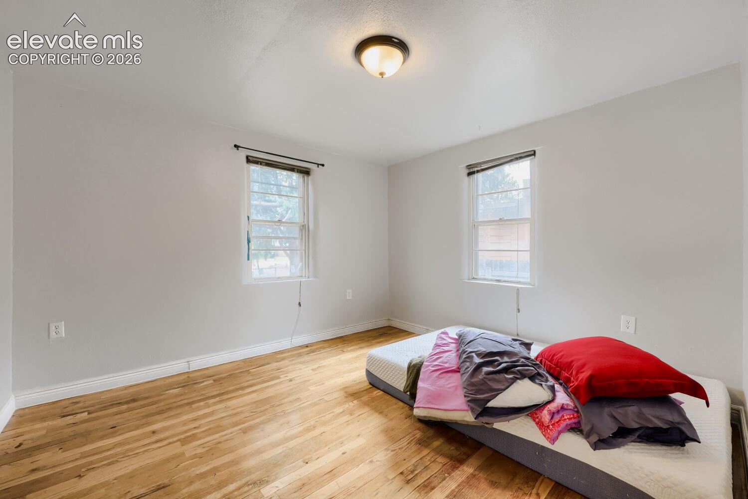 Hardwood flooring, light gray wall paint, two windows, ceiling-mounted light fixture, white trim