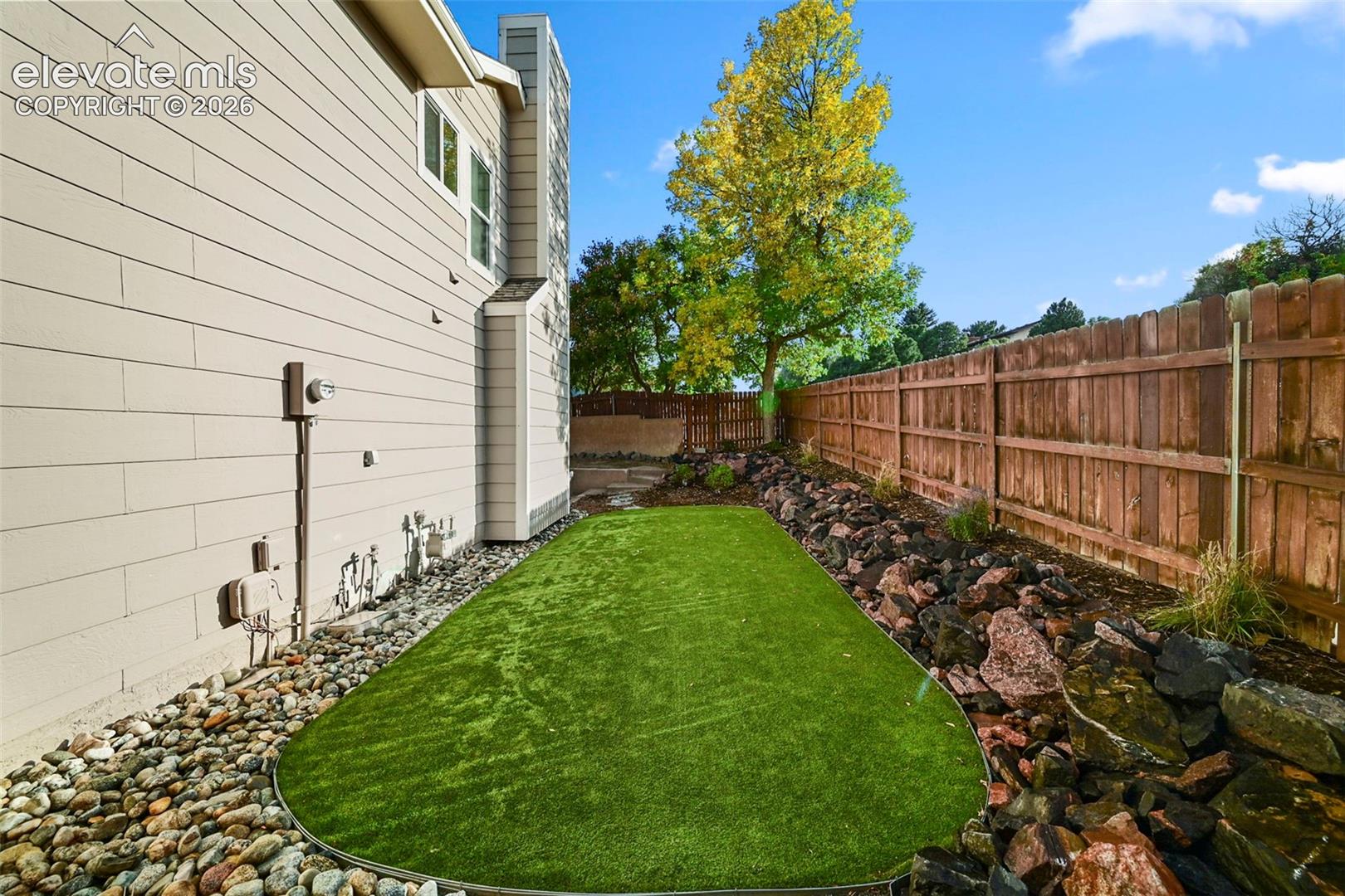 Exterior siding with windows, bordered by river rock and a vibrant artificial turf area