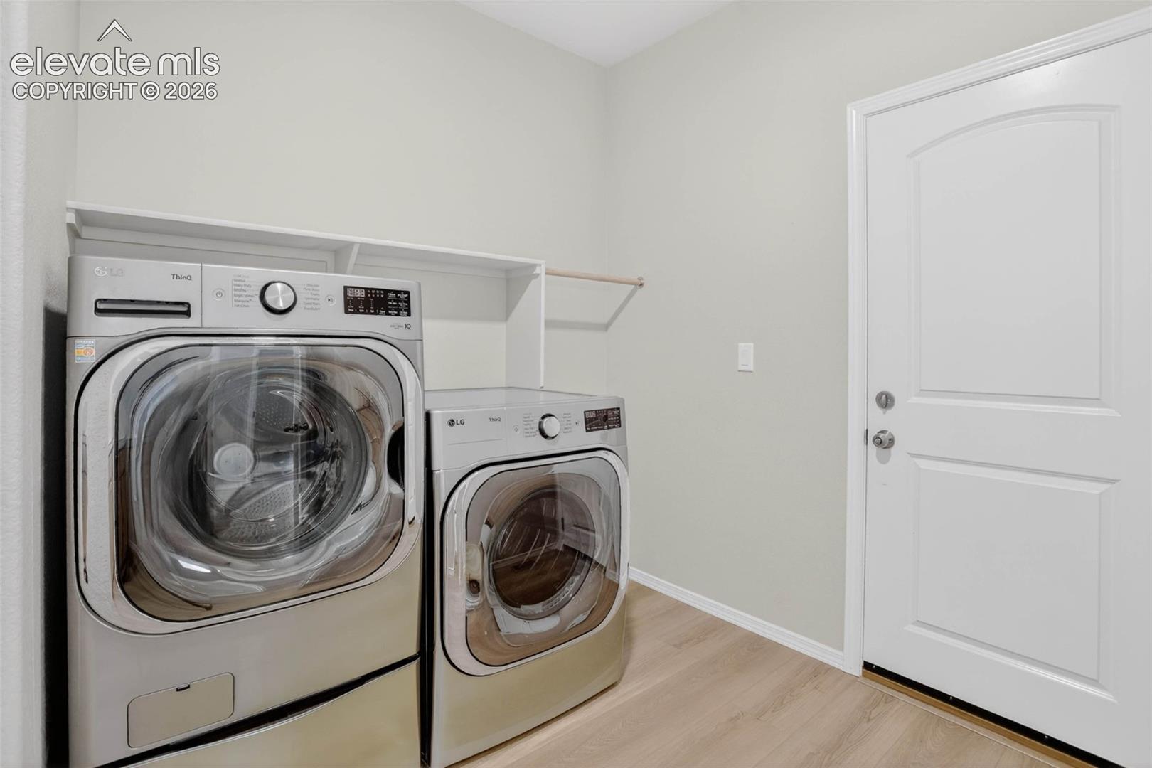 Utility room featuring light wood-finish flooring, light neutral wall paint, white trim, and a white paneled door with an arched top panel