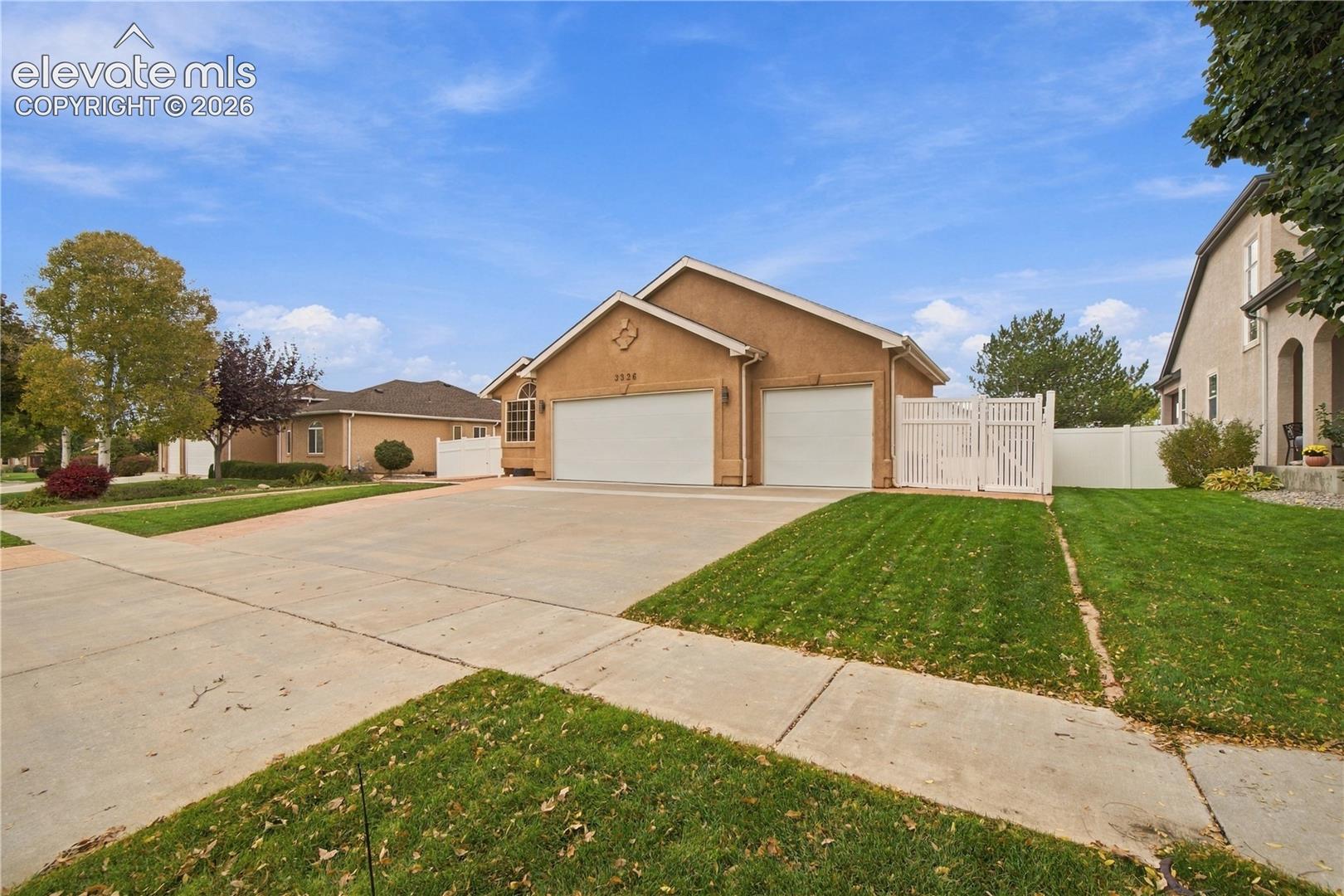 Stucco exterior featuring a three-car garage, concrete driveway, and white vinyl privacy fencing