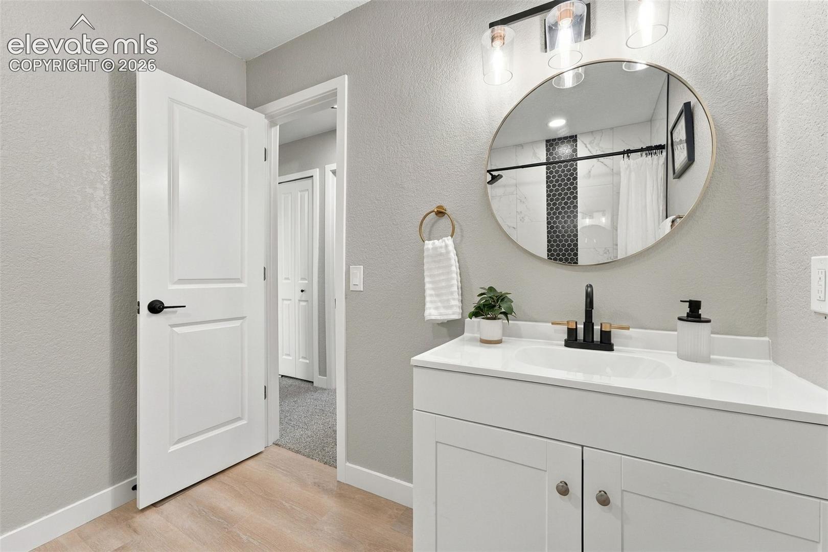 Bathroom featuring a white vanity with a composite countertop, round mirror, matte black faucet, and modern three-light wall fixture