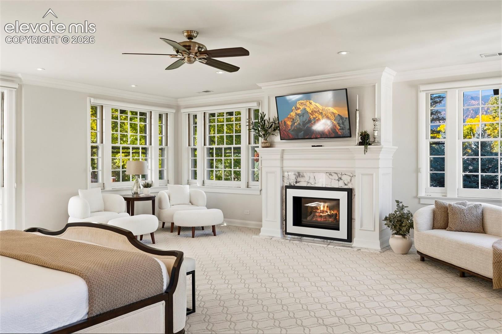 Fireplace featuring a stone surround and custom millwork mantel, multi-pane windows, and a ceiling fan with integrated lighting