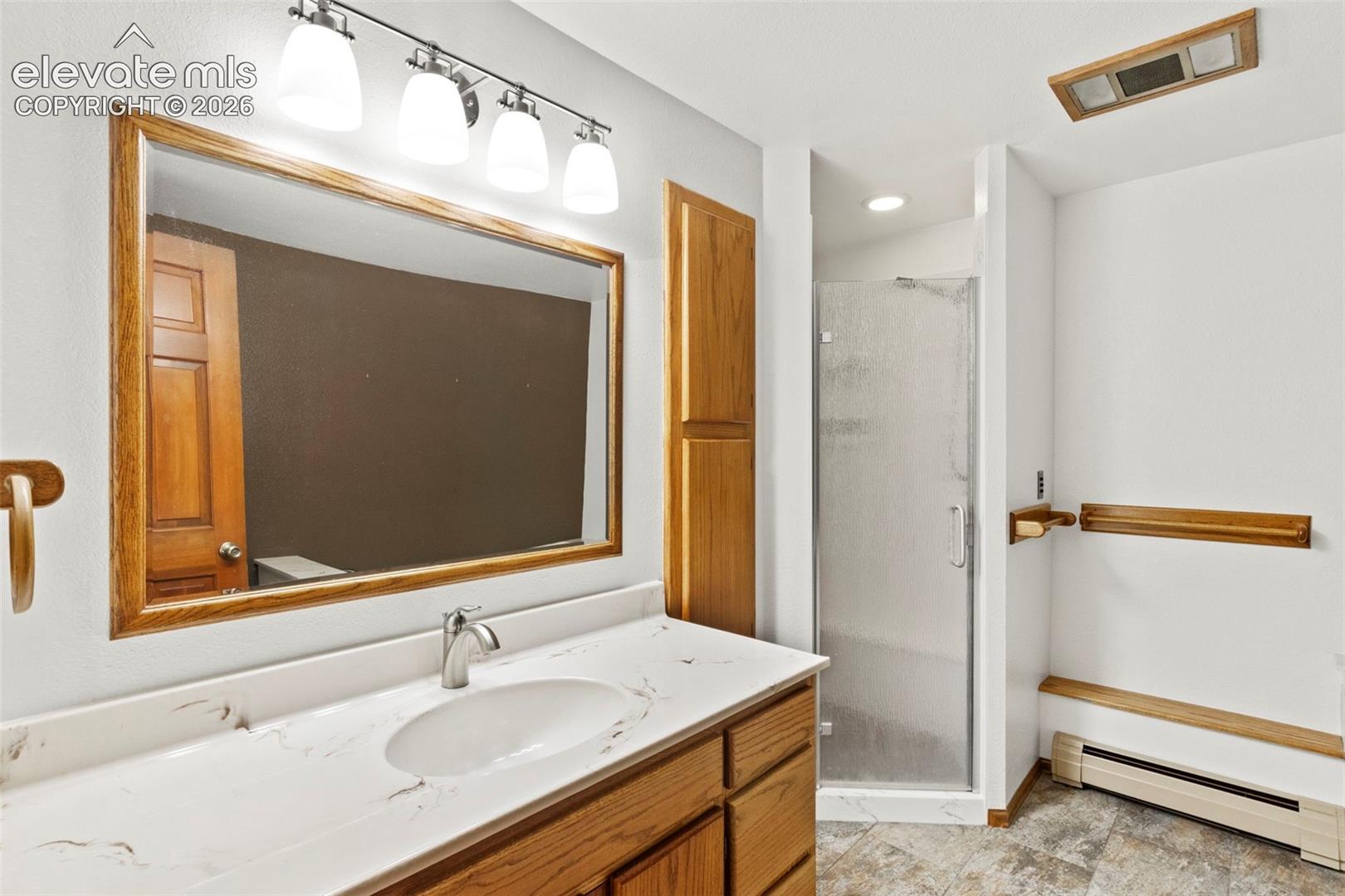 Bathroom featuring wood cabinetry, stone-surface countertop with an integrated basin, four-light vanity fixture, framed wall mirror, and a glass-enclosed shower stall