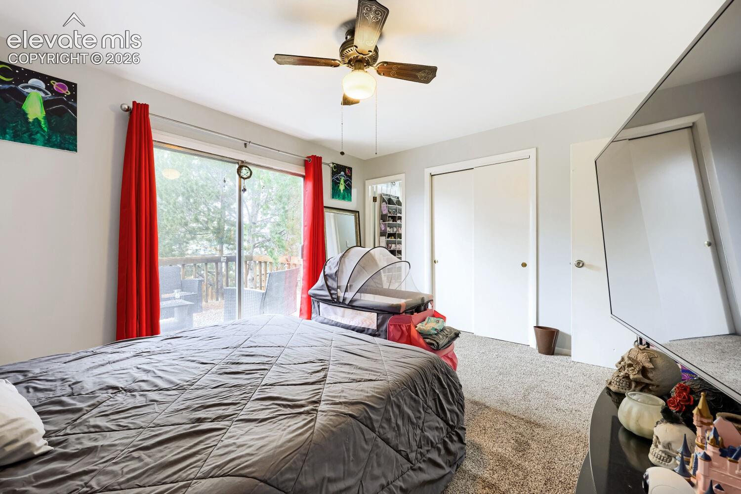 Carpeted flooring with a ceiling fan light fixture, double closet doors, and sliding glass door access to an exterior deck