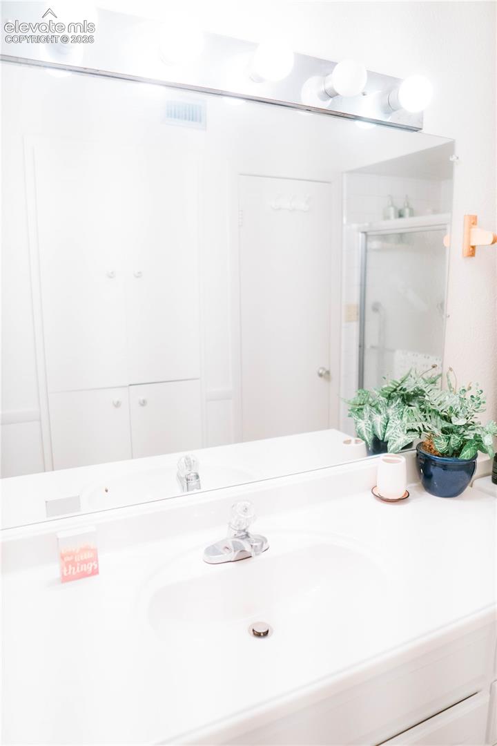 Vanity with an integrated sink, polished chrome faucet, and a large wall-mounted mirror with overhead lighting
