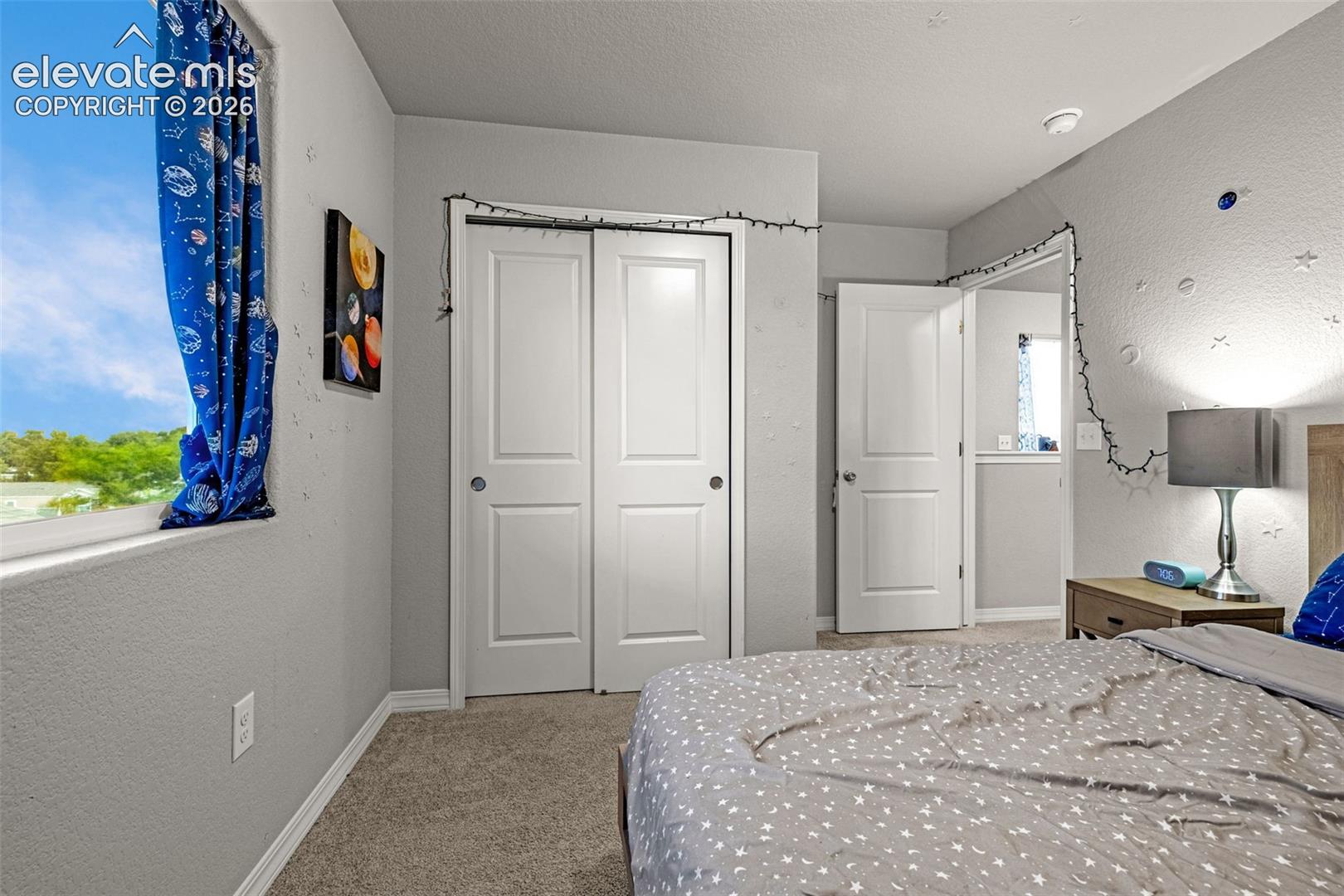 Bedroom featuring a double-pane window, bi-fold closet doors, textured walls, carpet flooring, and white baseboards