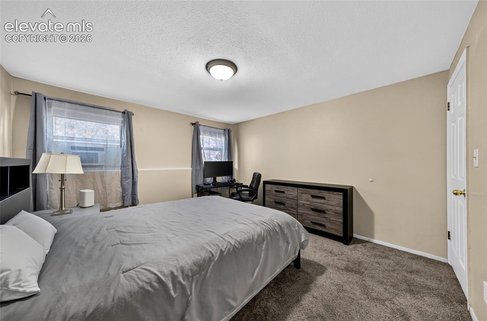 Neutral wall tones, dual windows featuring window air conditioning units, plush carpeting, and a flush-mount ceiling light fixture