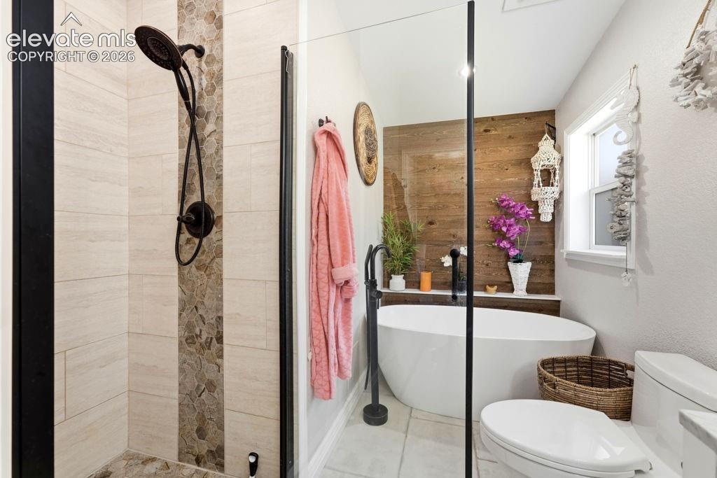 Freestanding soaking tub with a floor-mounted faucet, wood-finish accent wall, walk-in shower with stone and tile surround, and a toilet