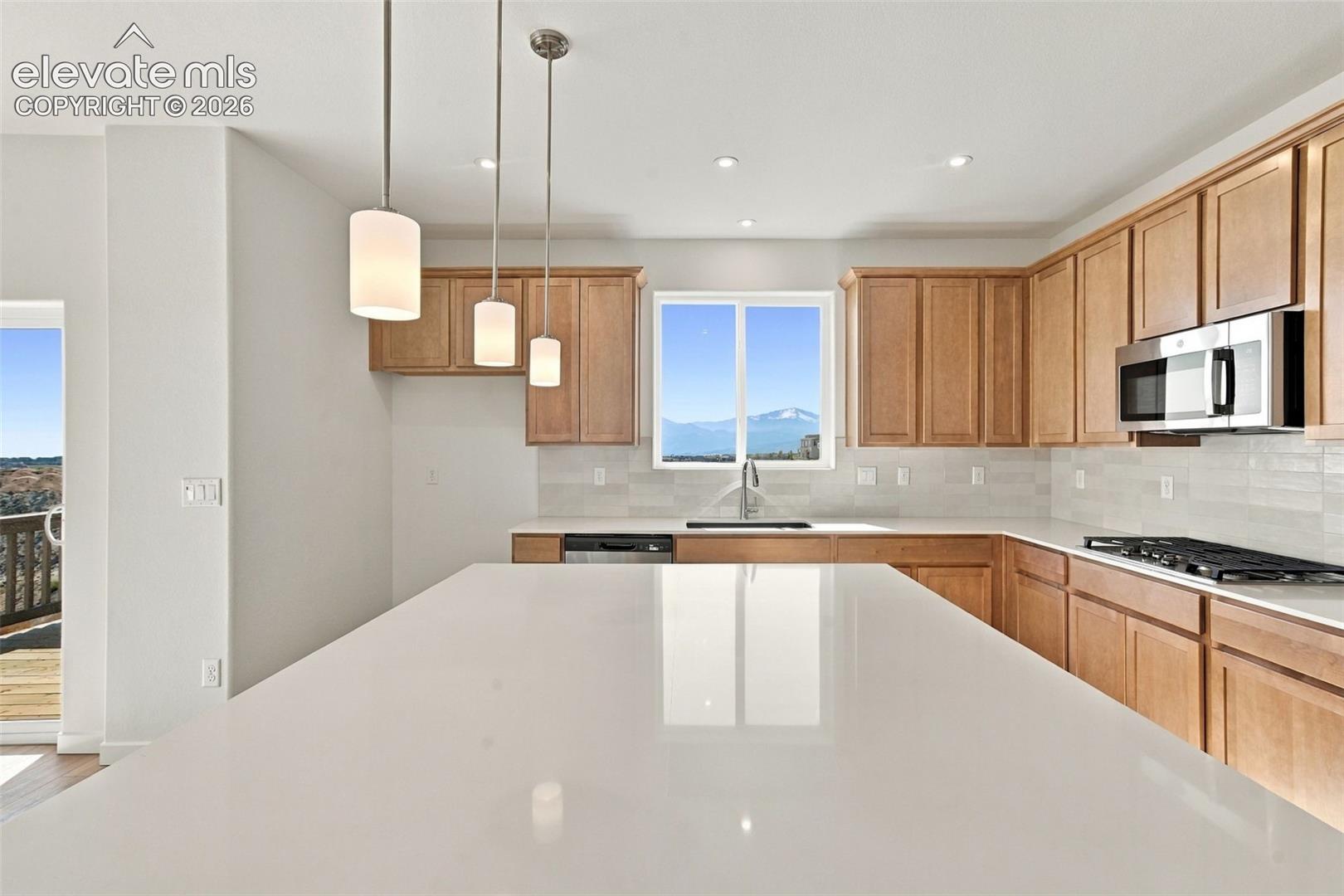 Kitchen featuring a large island with a white countertop, light wood-finish cabinetry, stainless steel microwave, and white subway tile backsplash