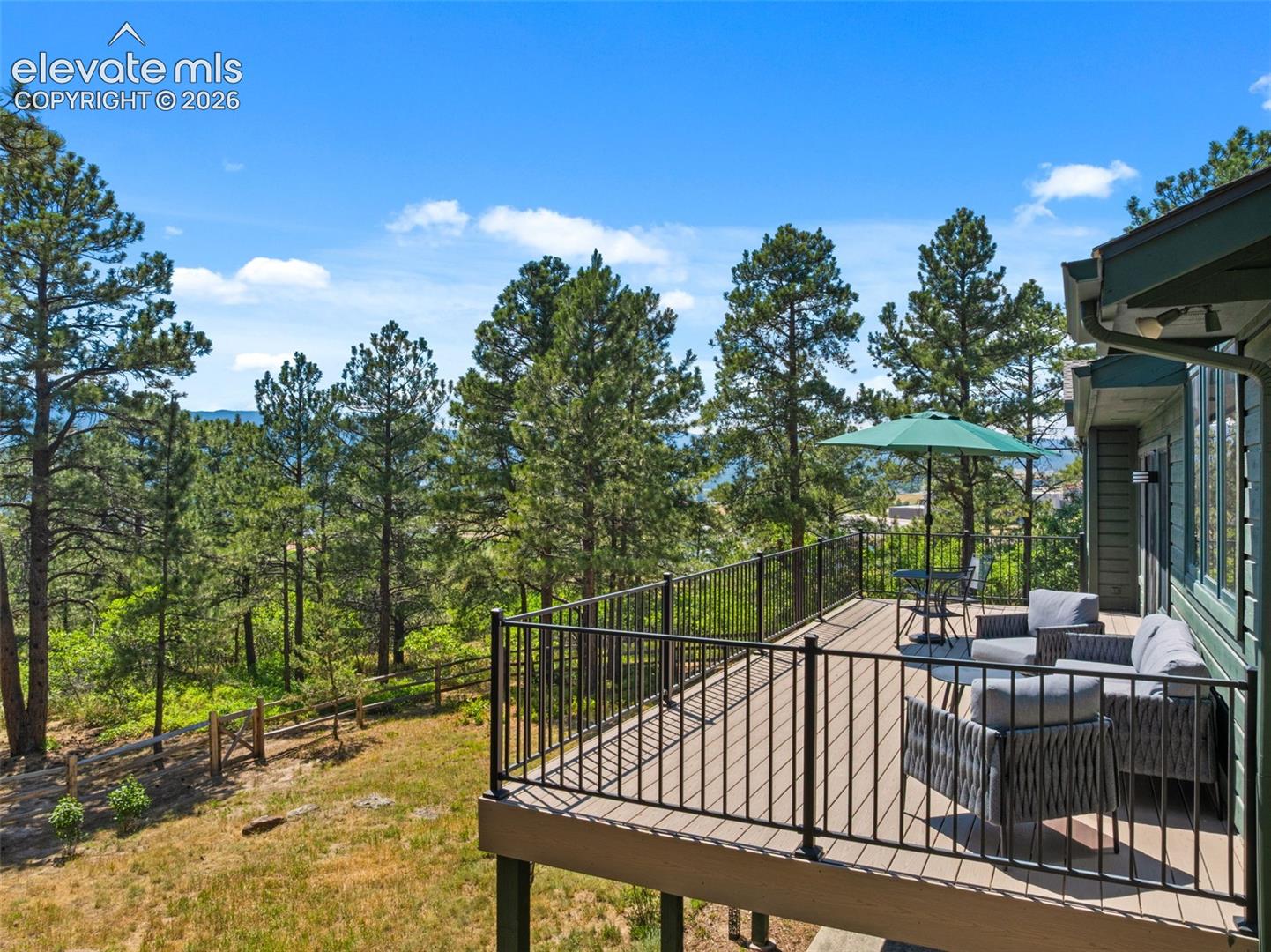 Spacious exterior deck featuring composite decking, black metal railings, and a serene treeline backdrop