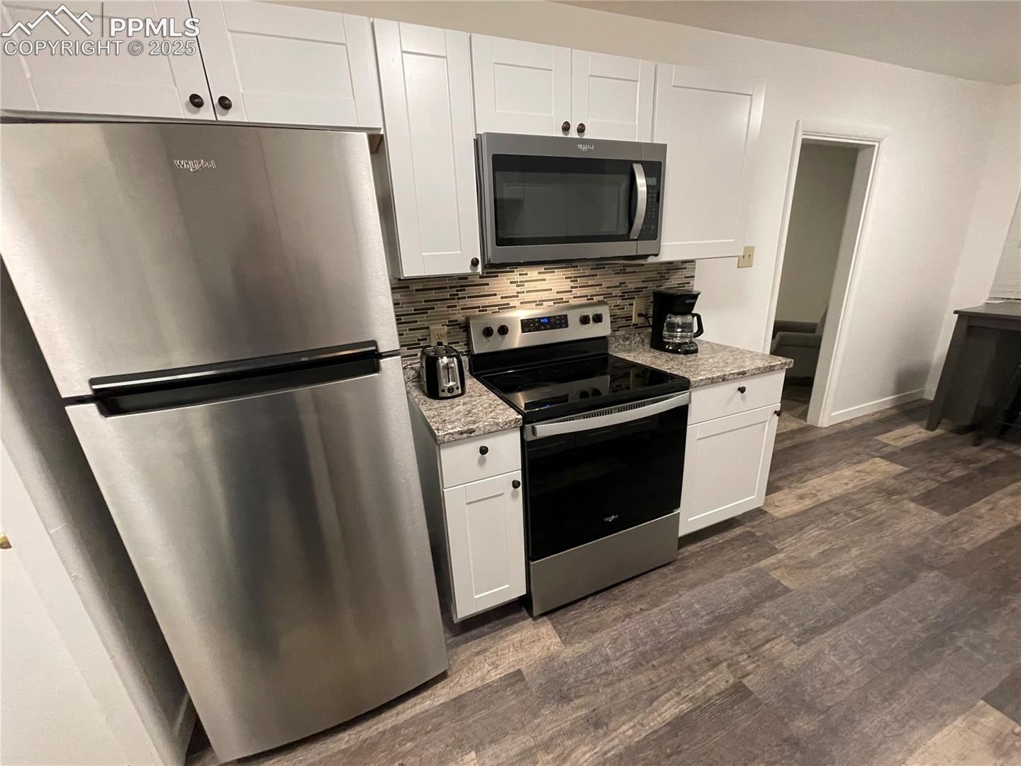 Kitchen featuring stainless steel appliances, white cabinetry, dark wood-style floors, and light stone countertops