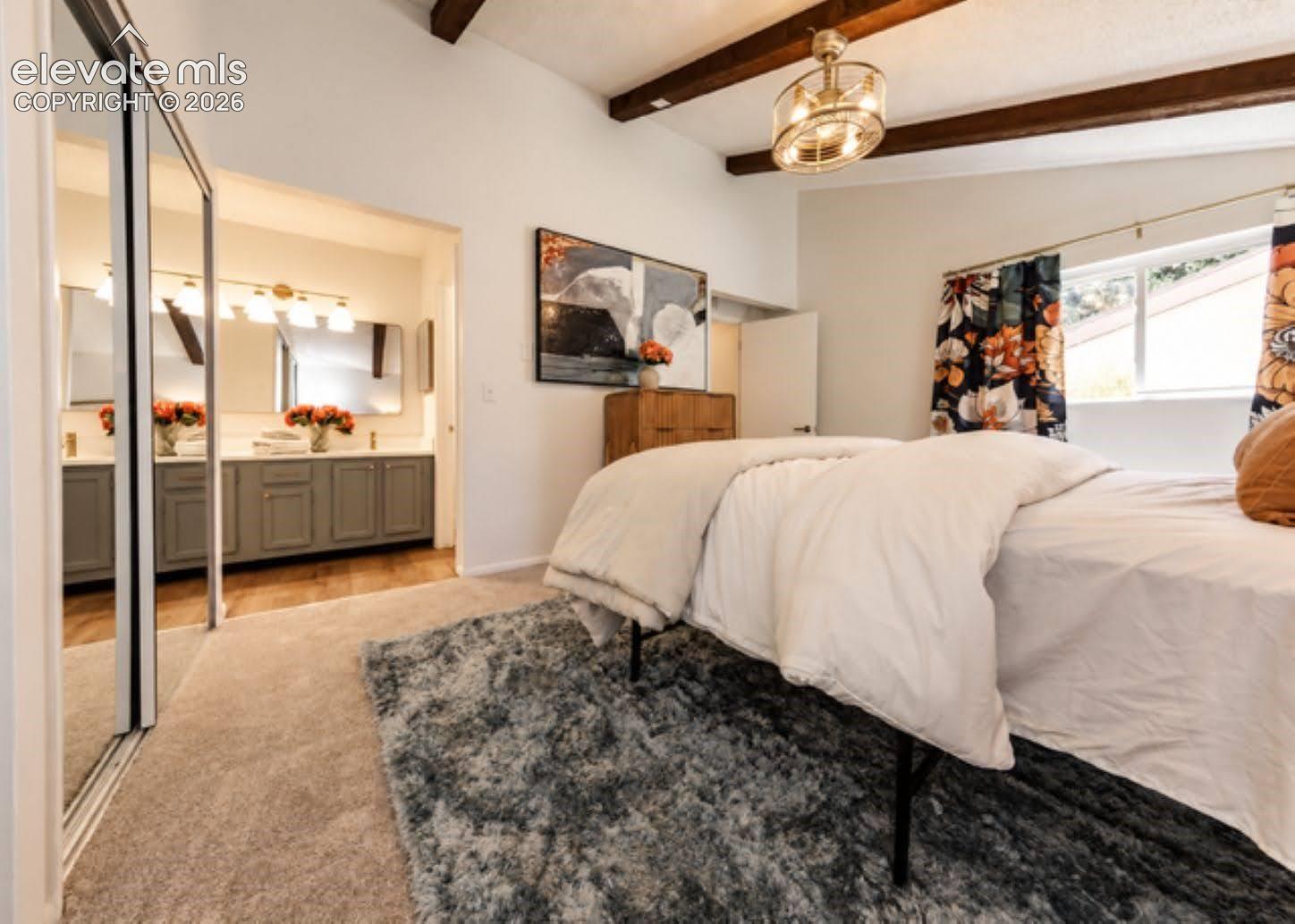 Vaulted ceiling with exposed wood beams, sliding mirrored closet doors, and attached multi-light ceiling fixture