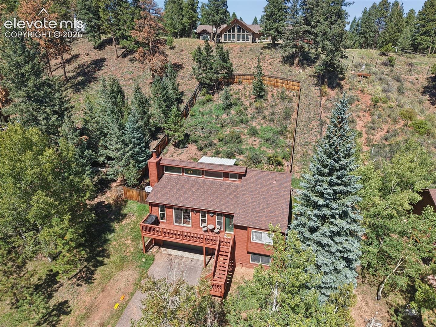 Sloped lot with mature evergreen trees, a multi-level deck, and a fenced area