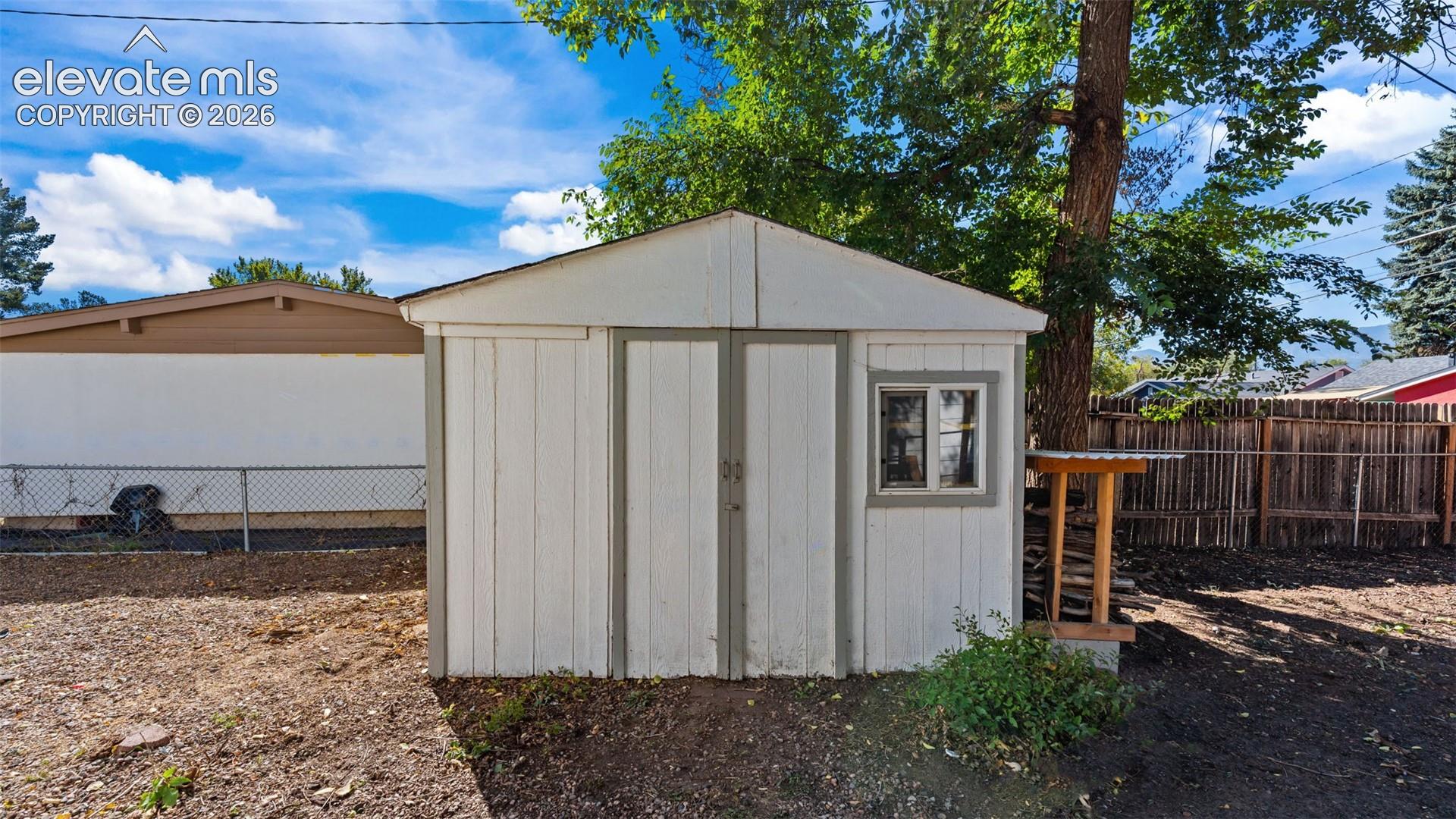 Detached storage shed featuring white vertical paneling, dual entry doors, a single window, and a gabled roof