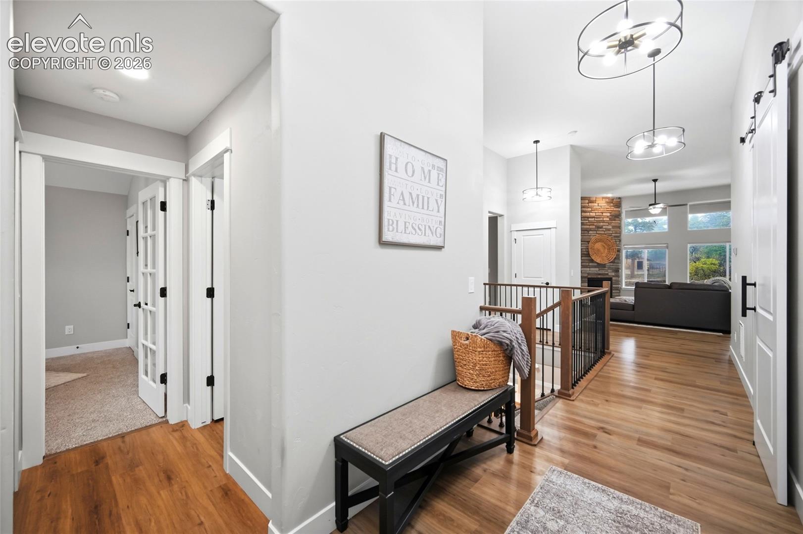 Interior hallway featuring wood-finish flooring, sliding barn door, stone-accented wall, recessed lighting, and multi-tier iron chandeliers