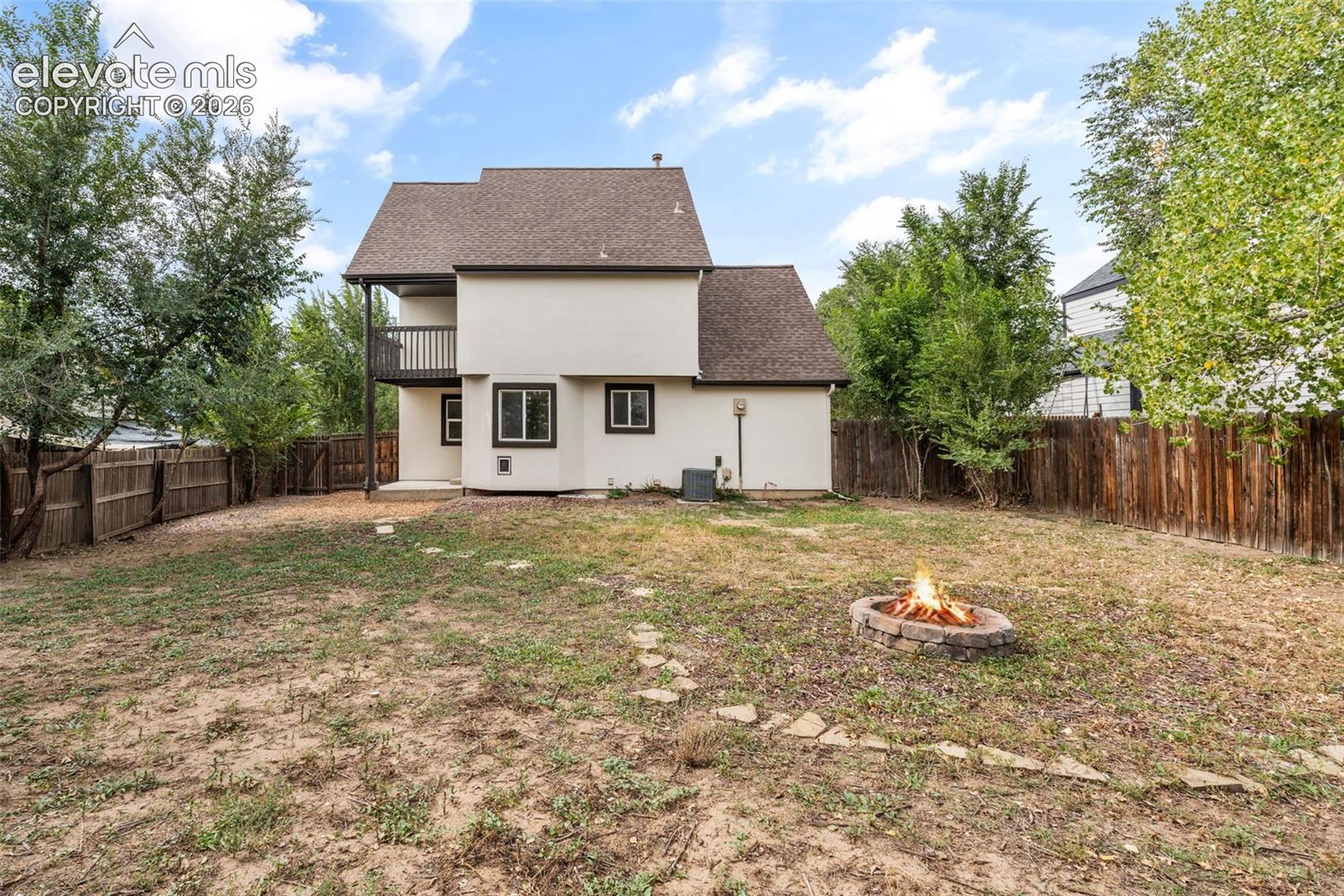 Backyard featuring a stone-encased fire pit, a covered second-story balcony, and wood-style perimeter fencing