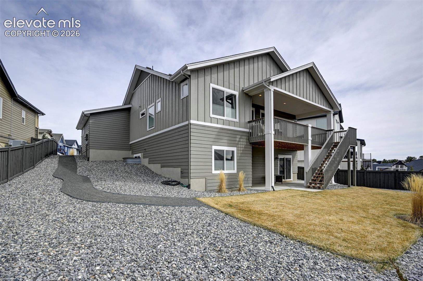 Gray siding exterior with multi-level covered deck, privacy fencing, and gravel landscaping