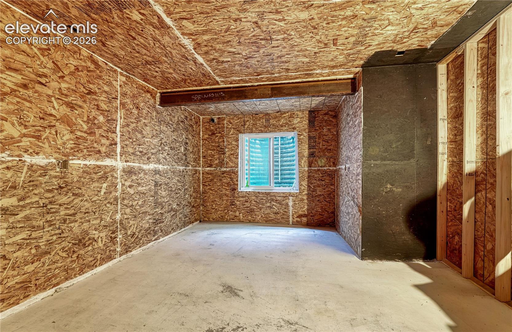 Unfinished room with concrete flooring, oriented strand board walls and ceiling, a single window, and visible structural beams