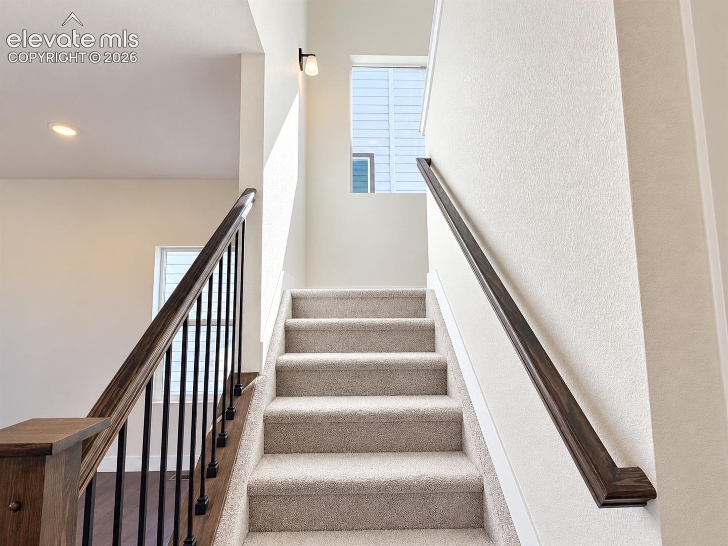 Carpeted stairway with dark wood handrails and black balusters