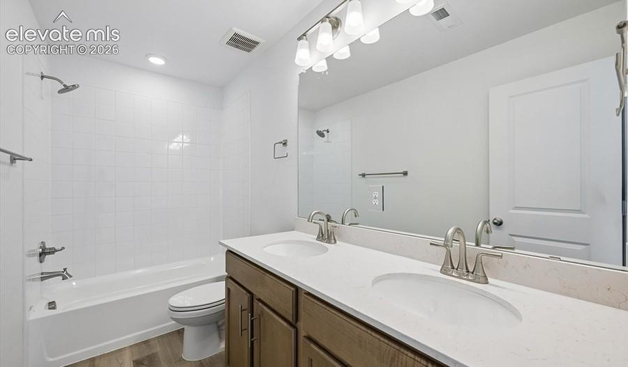 Bathroom featuring a double vanity with stone-composite countertop, dual undermount sinks, wood-finish cabinetry, and a full-width wall mirror