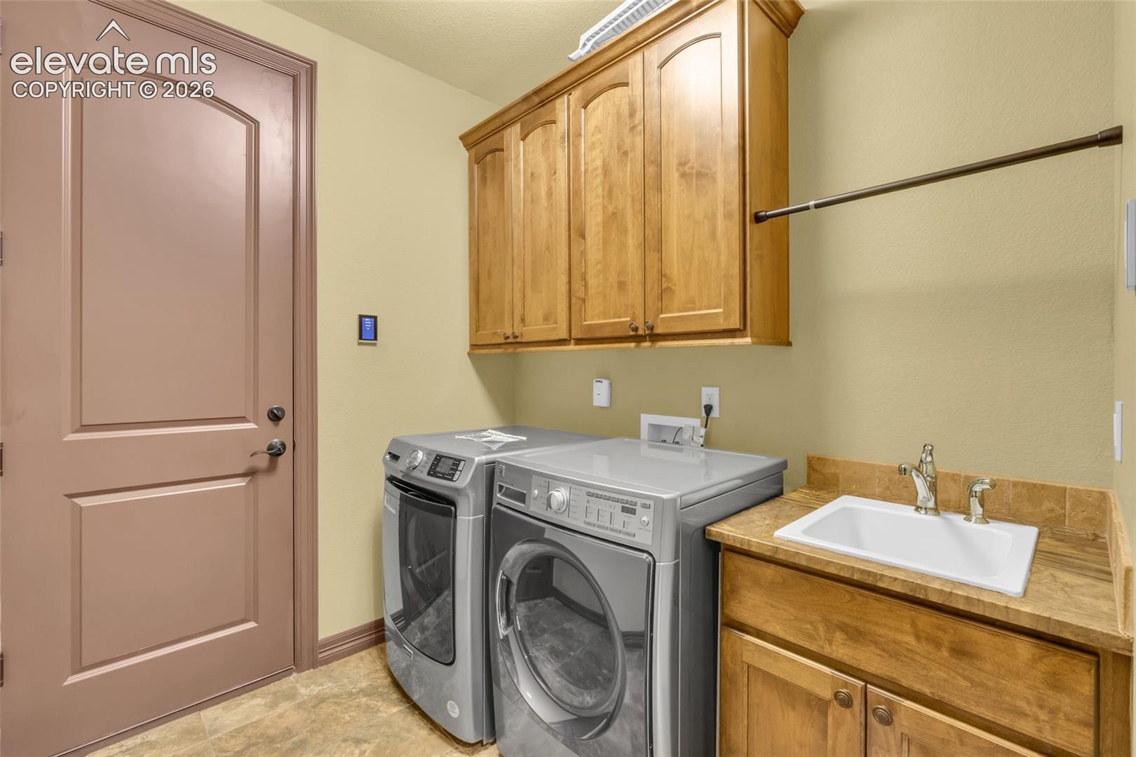 Utility area featuring wood-finish cabinetry, a drop-in sink with a high-arc faucet, solid-surface countertops, and a wall-mounted hanging rod
