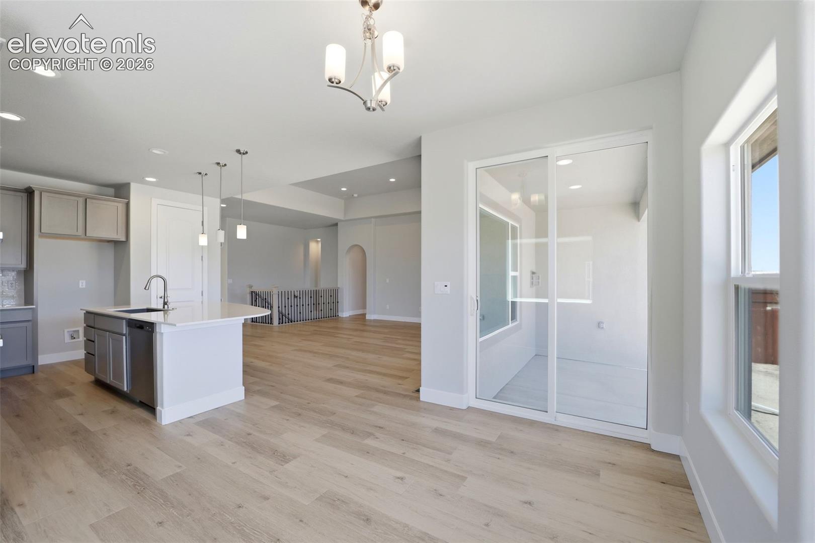 Kitchen featuring a central island with a solid-surface countertop and stainless steel faucet, wood-finish flooring, glass sliding doors, recessed lighting, and a multi-arm chandelier