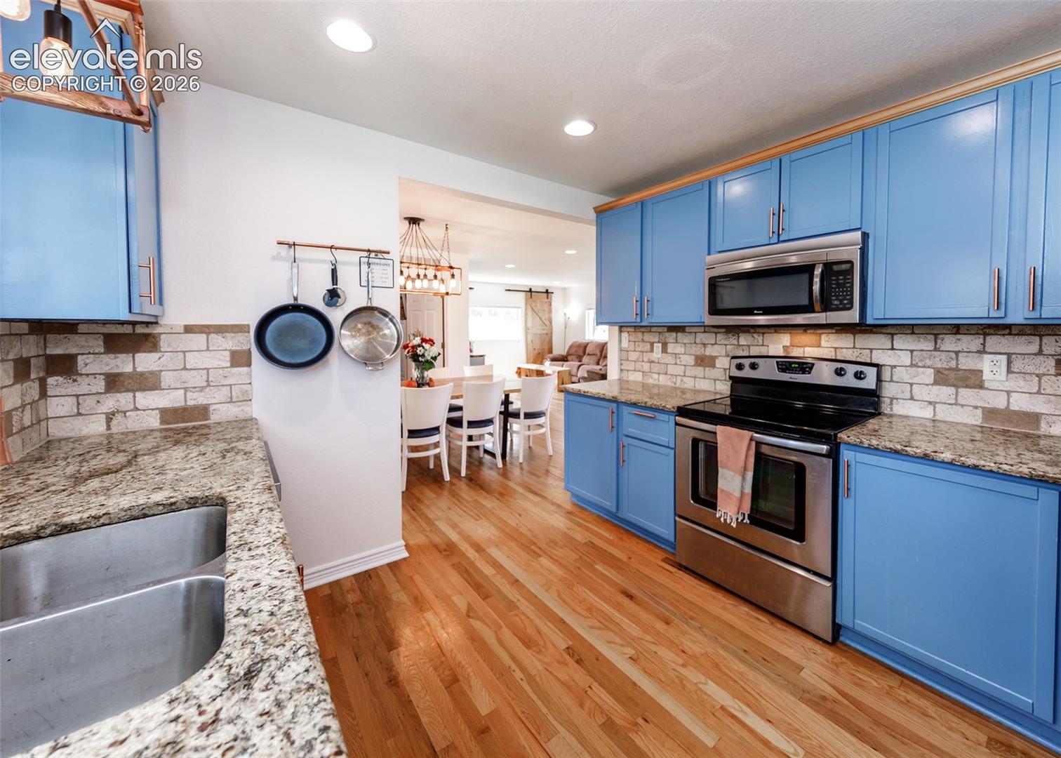 Kitchen with wood-finish flooring, vibrant blue cabinetry, stainless steel appliances, a double basin sink, and stone countertops