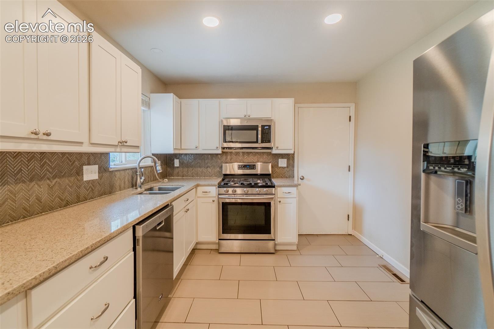 White cabinetry, stainless steel appliances, patterned tile backsplash, light-toned countertops, and tiled flooring