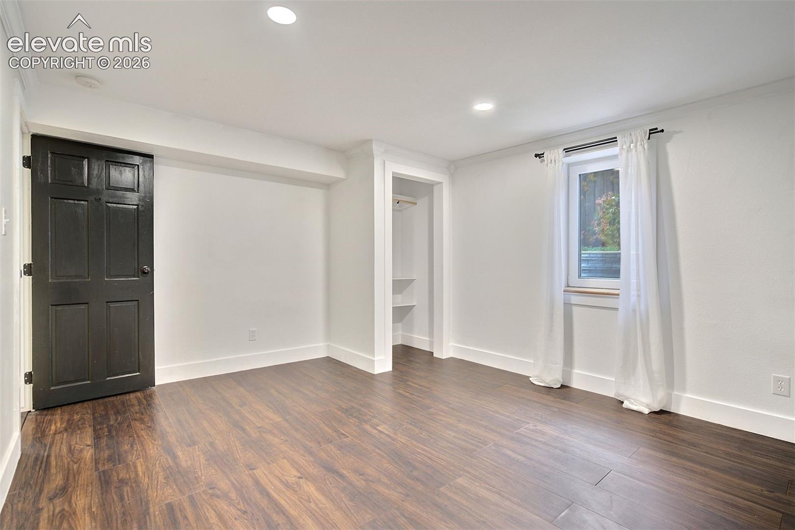 Room featuring wood-finish flooring, recessed lighting, a high-contrast dark interior door, and a built-in closet with integrated shelving