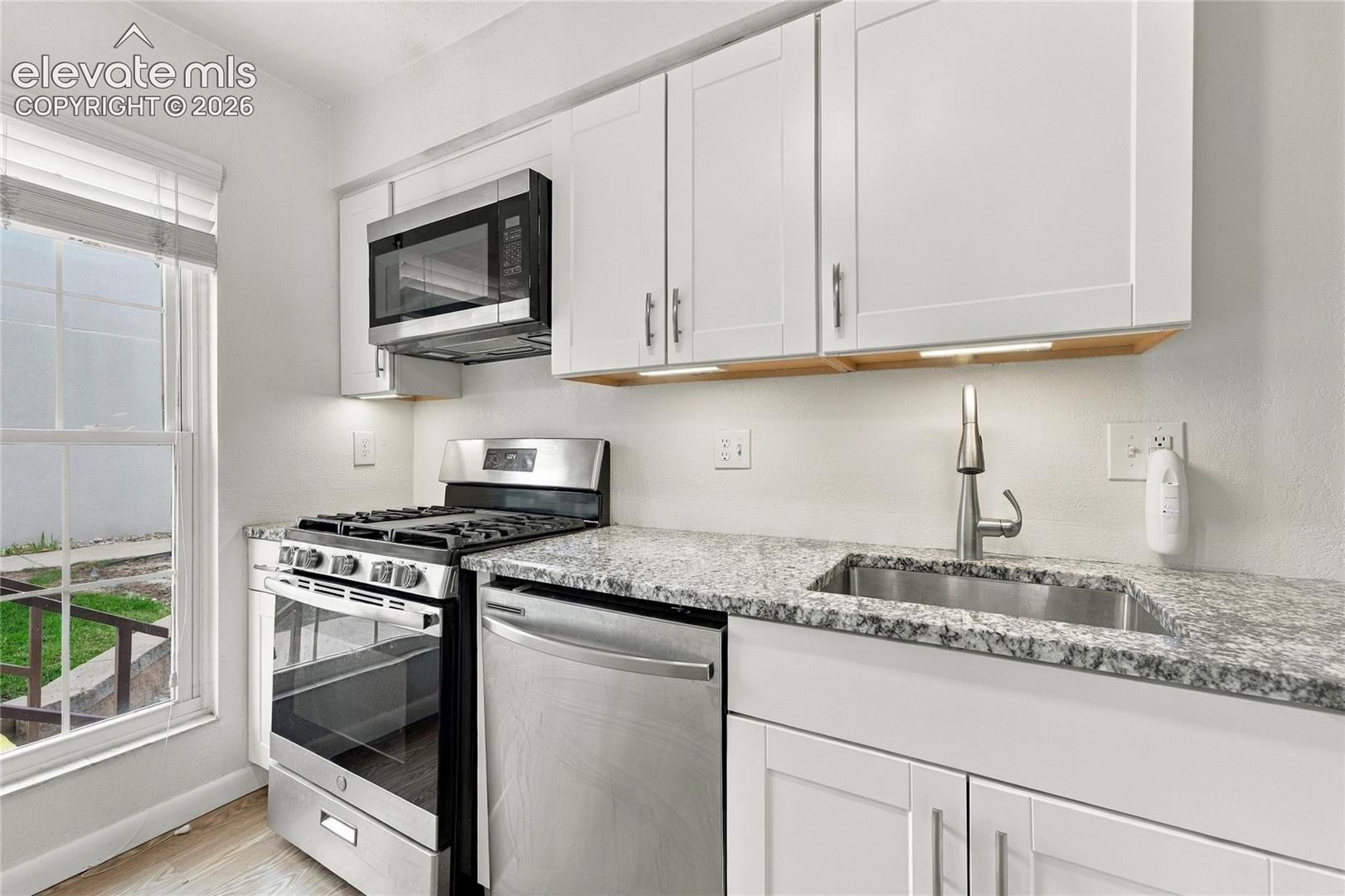 Kitchen featuring white shaker-style cabinetry, stone-patterned countertops, stainless steel appliances, and a single-basin undermount sink with a pull-down faucet