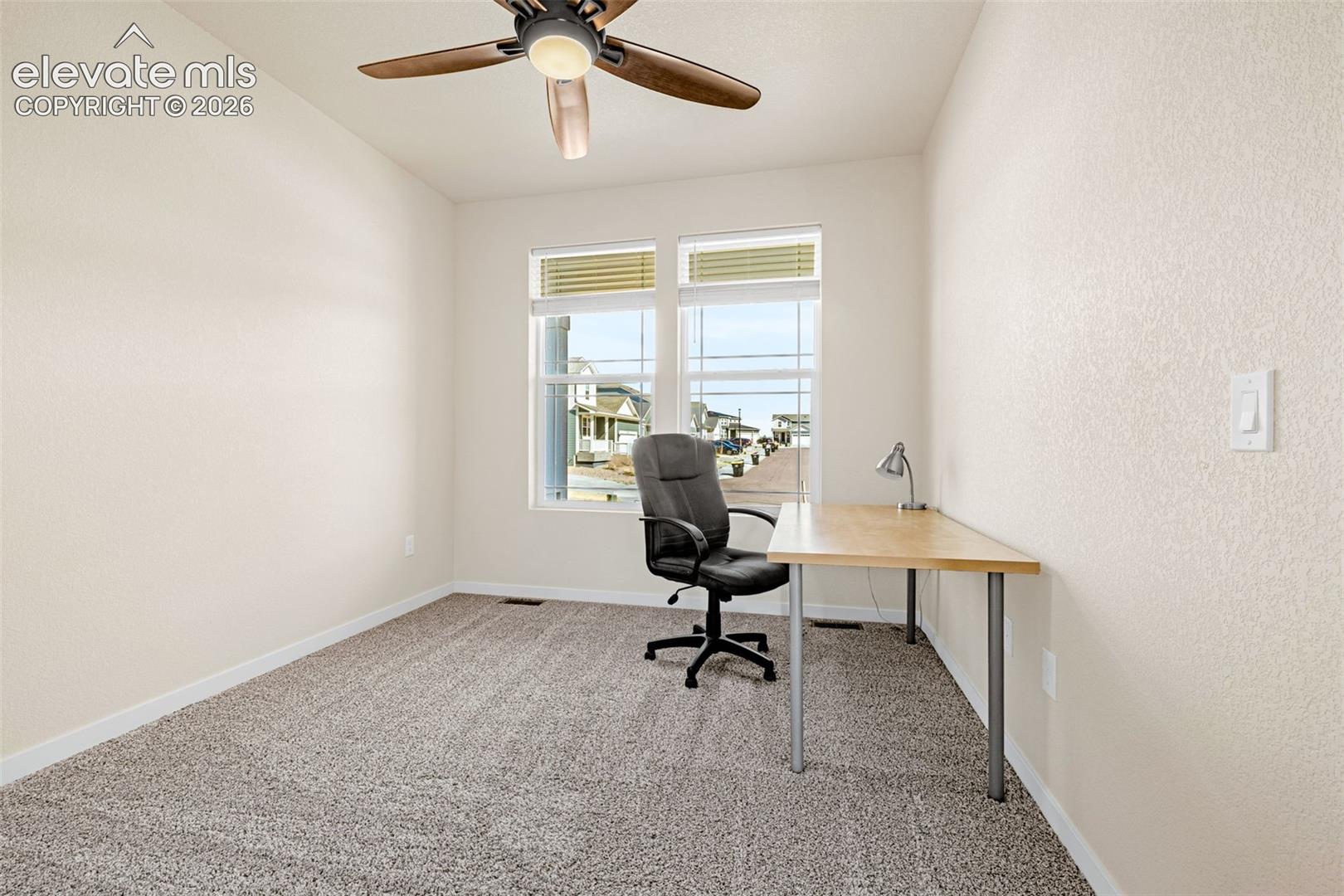 Neutral tone wall finish, textured carpet flooring, window with blinds, and a ceiling fan with integrated lighting