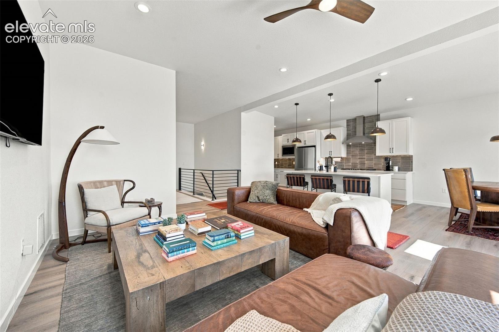 Open-concept area featuring wood-finish flooring, recessed lighting, a modern ceiling fan, a kitchen island with pendant lighting, and a neutral-toned tile backsplash