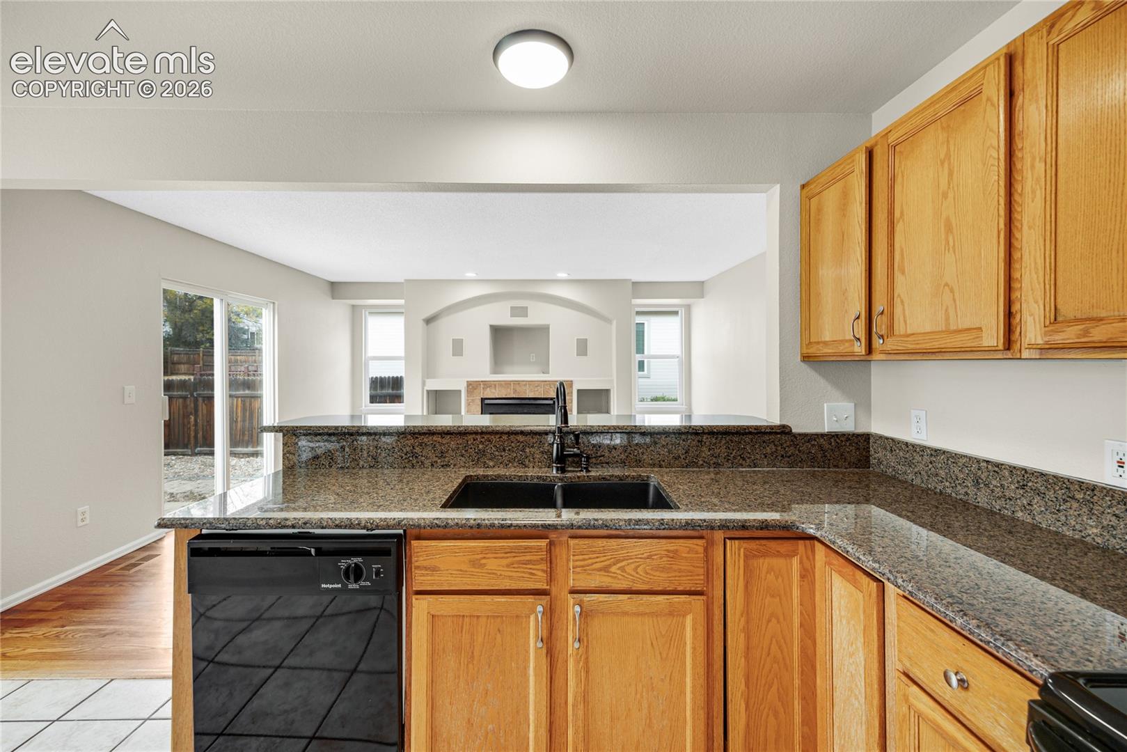 Kitchen featuring natural wood cabinetry, stone-surface countertops, an integrated undermount sink, and a black dishwasher
