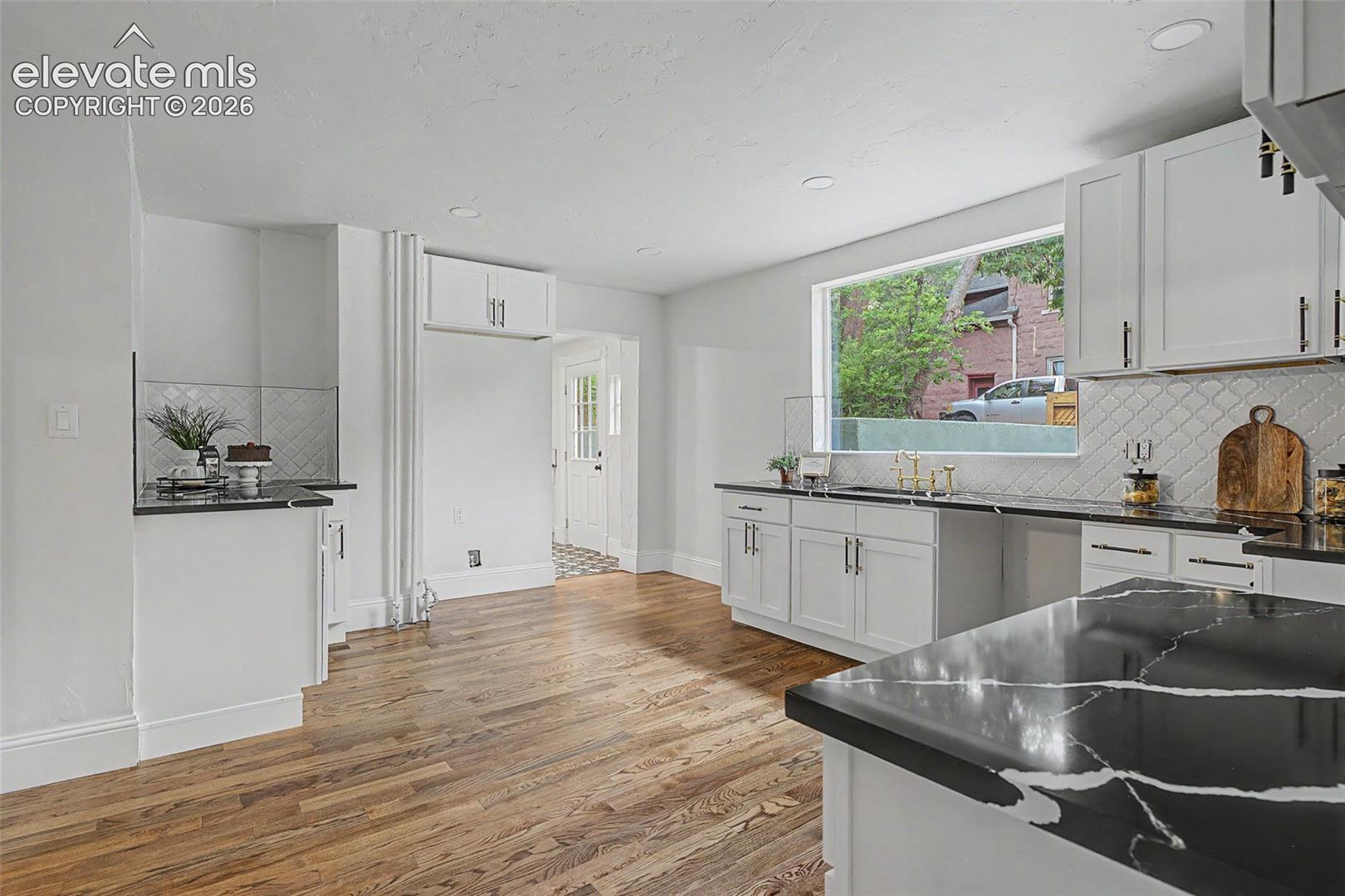 Spacious kitchen featuring expansive wood-finish flooring, white cabinetry, a large picture window, and striking black countertops