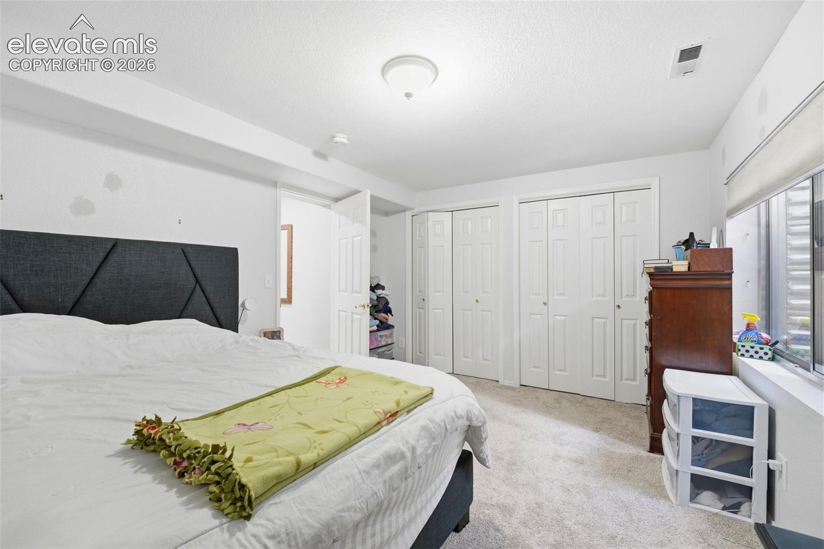 Carpeted room featuring multiple bi-fold closet doors, a window with a deep sill, and a flush-mount ceiling light fixture