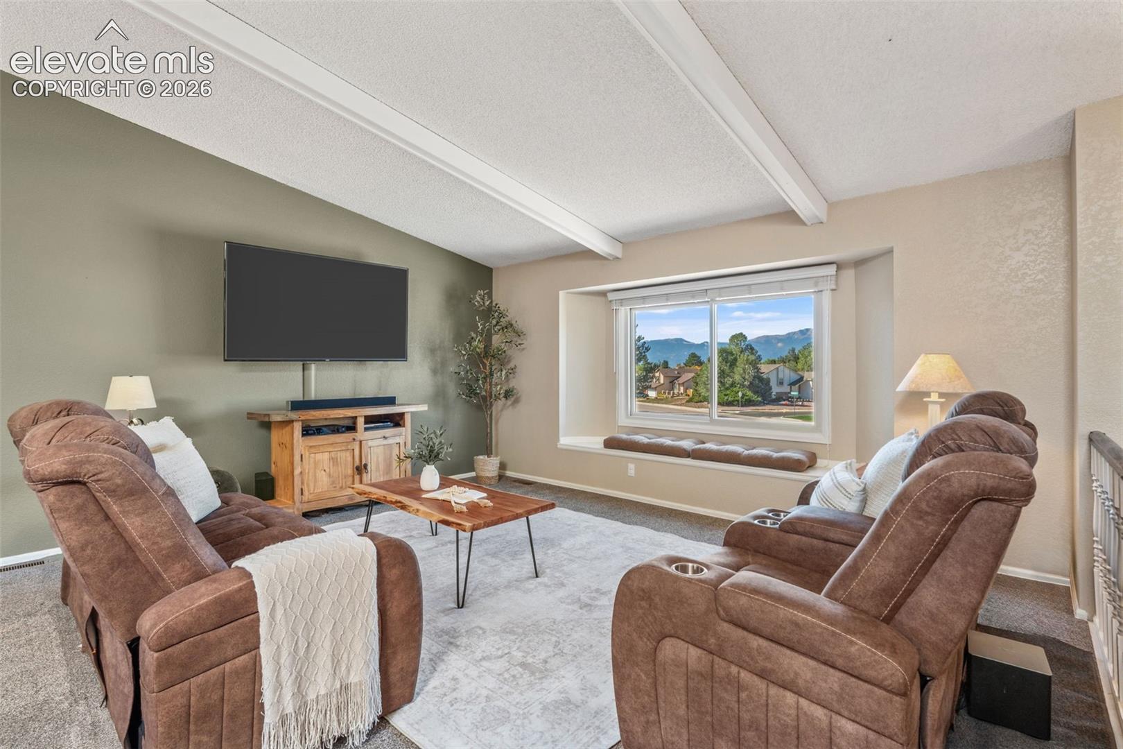 Vaulted ceiling with exposed beams, bay window with integrated seating, and mountain backdrop