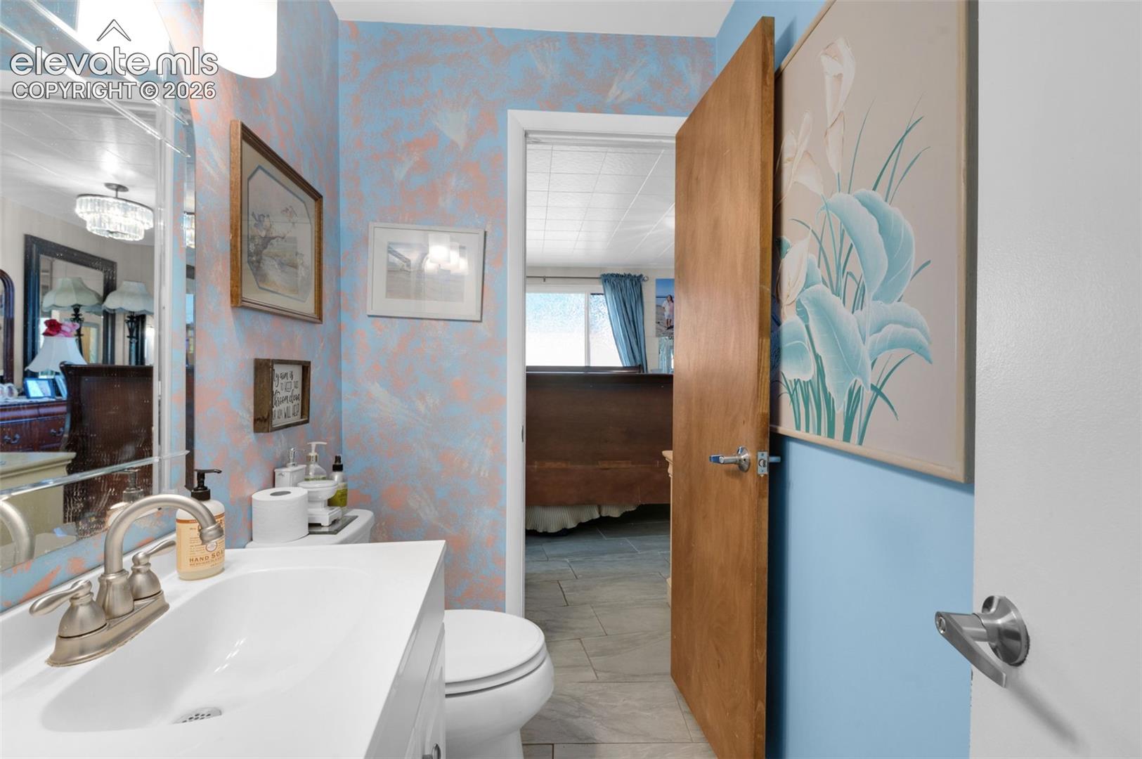 Bathroom featuring a white vanity with an integrated basin, high-arch polished chrome faucet, wall-mounted light fixture, and tile flooring