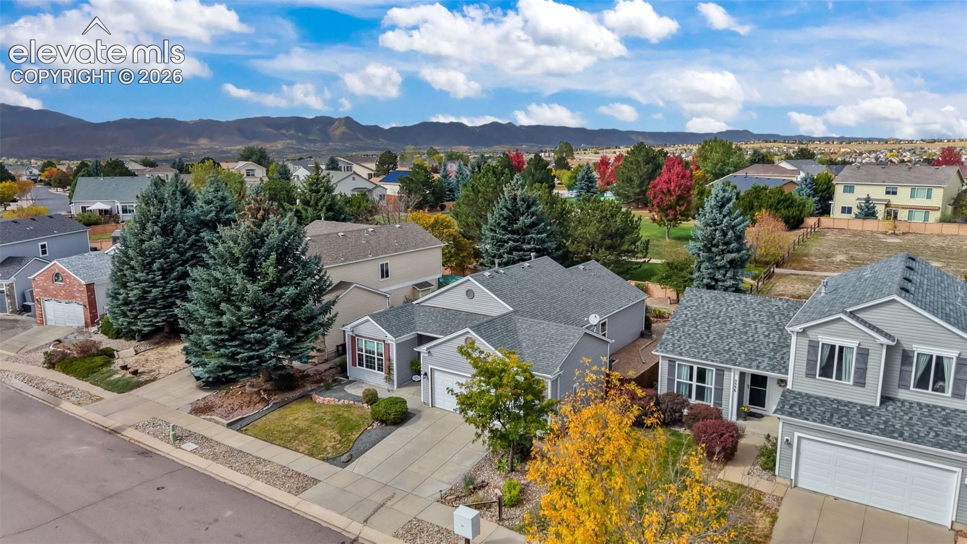 Aerial perspective featuring gray-toned siding, asphalt shingle roofing, attached multi-car garages, mature evergreen trees, and a mountain backdrop