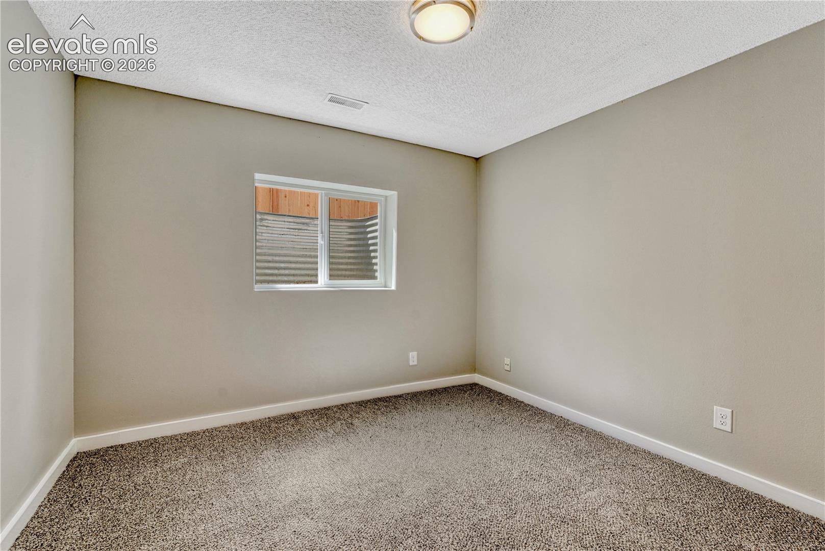 Neutral wall color, wall-to-wall carpeting, window with a window well, and a flush-mount ceiling light