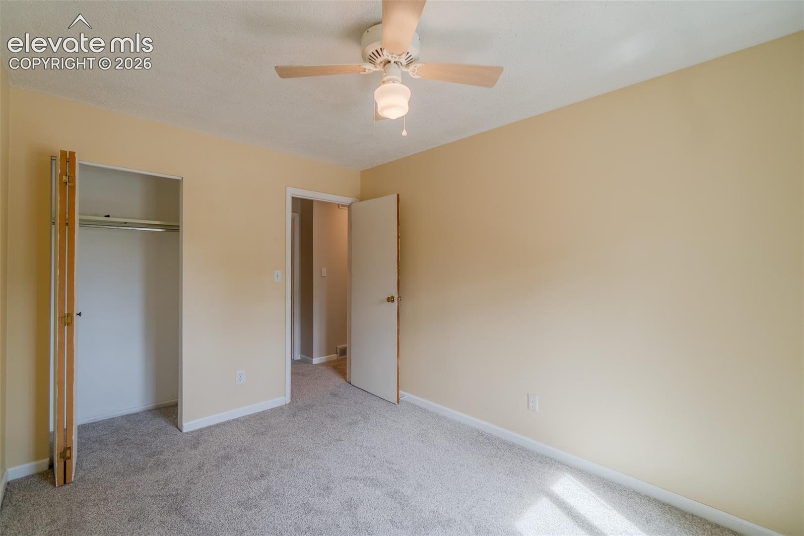 Carpeted flooring, neutral wall tones, ceiling fan with light fixture, built-in closet with bifold doors, and a solid core door