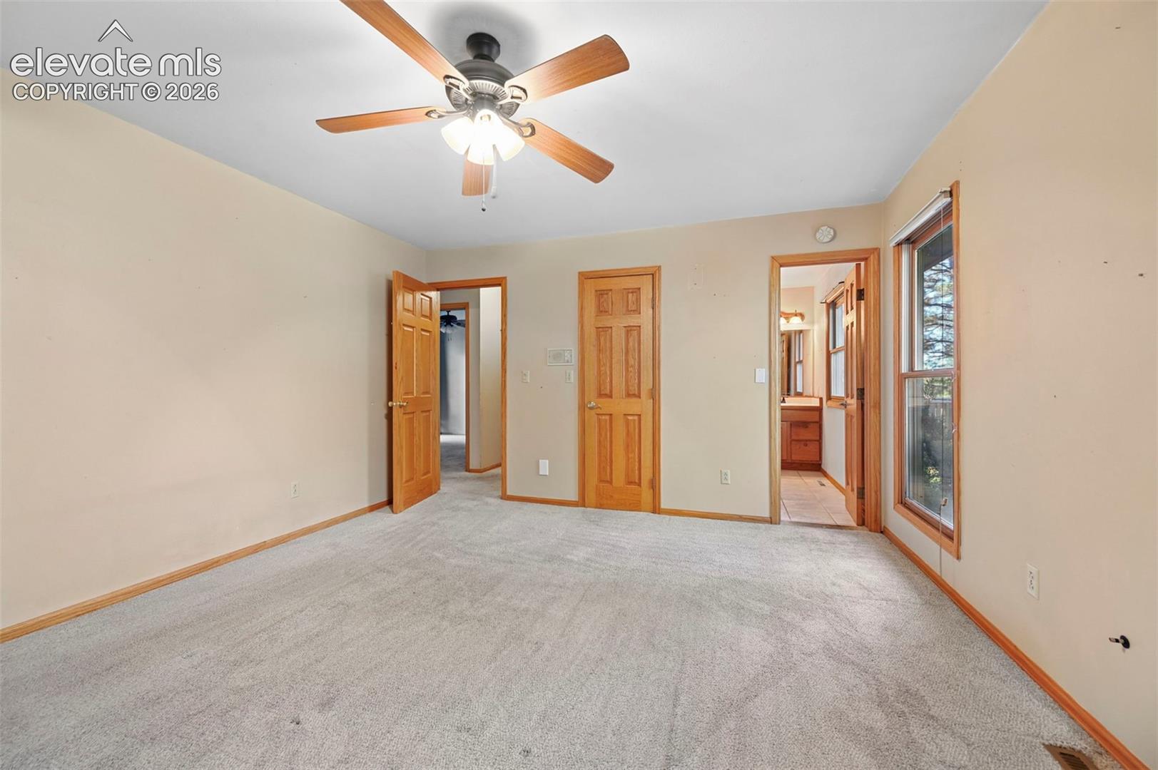 Carpeted room featuring a ceiling fan with integrated lighting, wood-finish interior doors, and a window with wood trim
