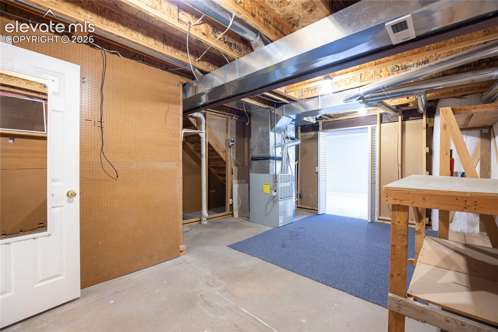 Unfinished lower level featuring exposed joist ceilings, concrete flooring, pegboard wall panels, and a dedicated furnace system