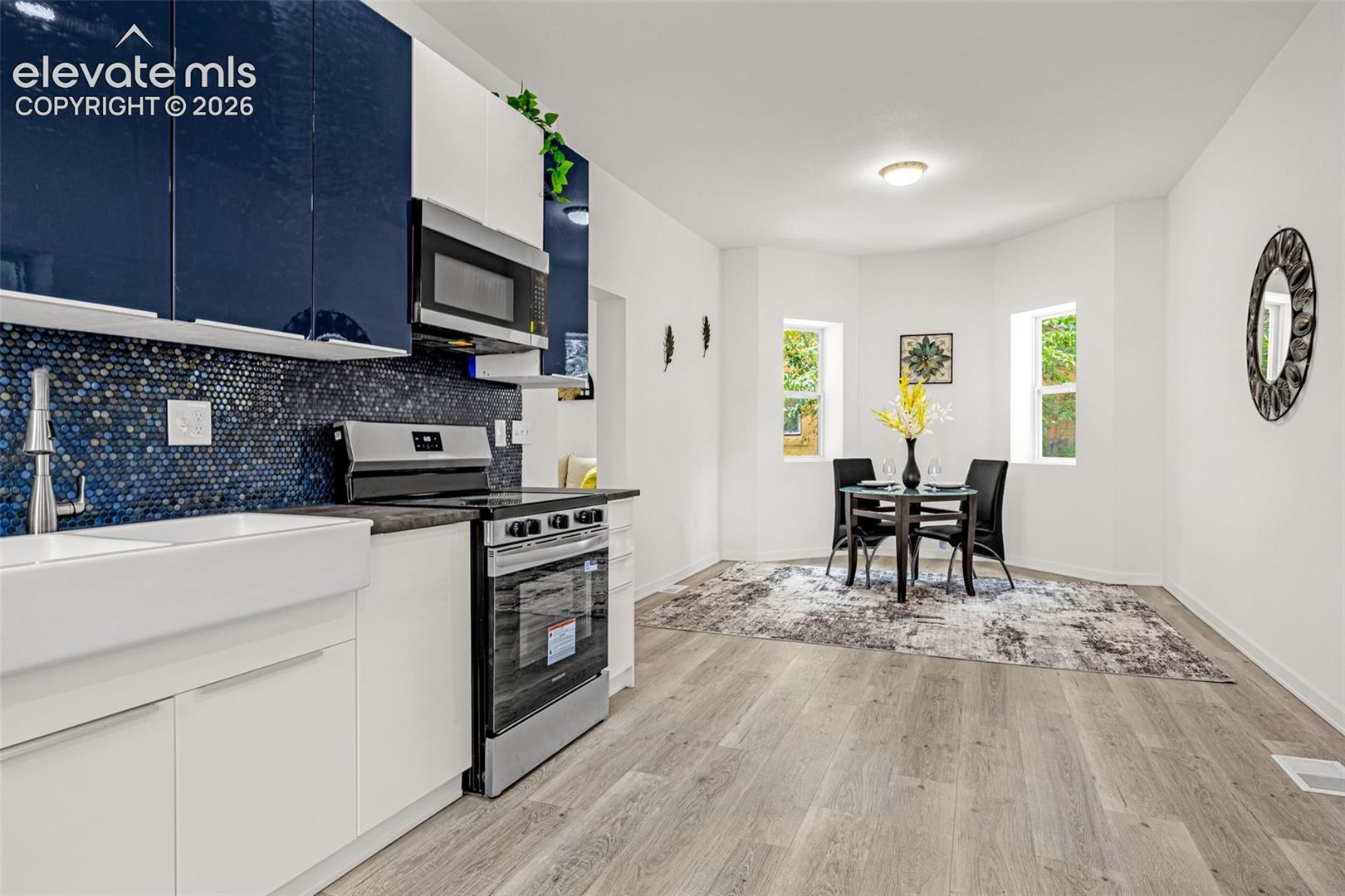 Contemporary kitchen featuring white and navy cabinetry, a blue penny tile backsplash, stainless steel appliances, and a farmhouse sink