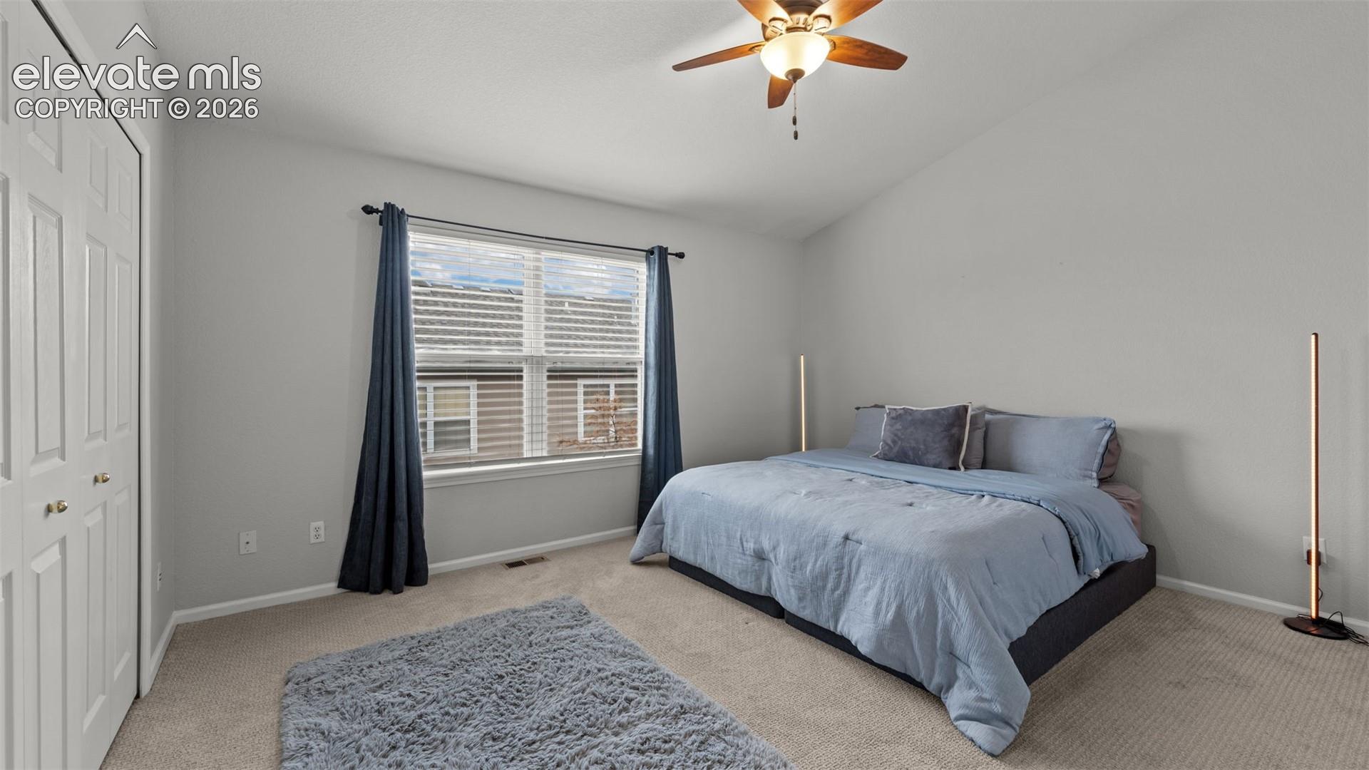 Vaulted ceiling, neutral wall tones, carpeted flooring, double-door closet, and a central ceiling fan with integrated lighting