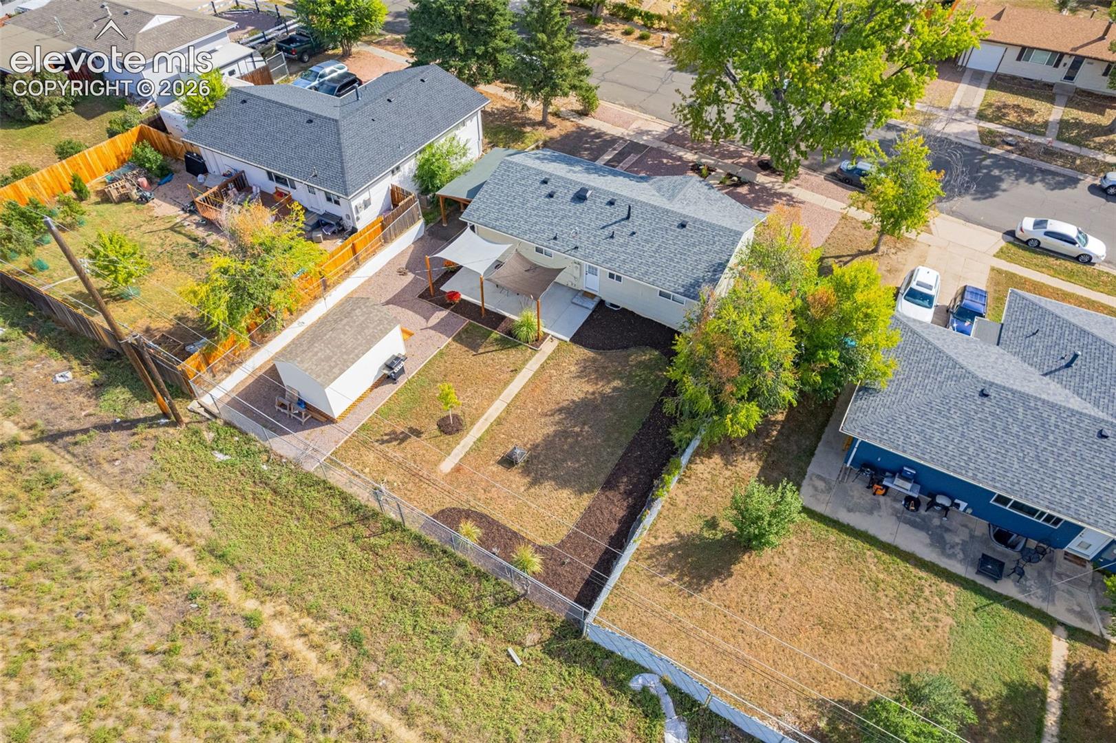 Expansive fenced backyard with a detached shed, crushed asphalt driveway, and mature trees