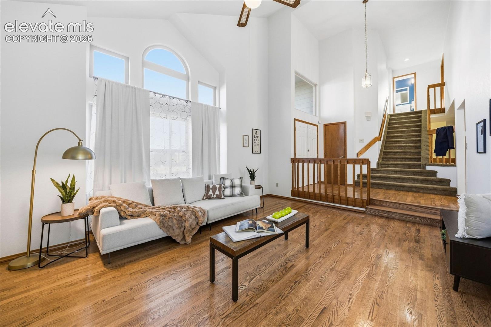 Vaulted ceilings with large arched windows, wood-finish flooring, and wooden staircase railing