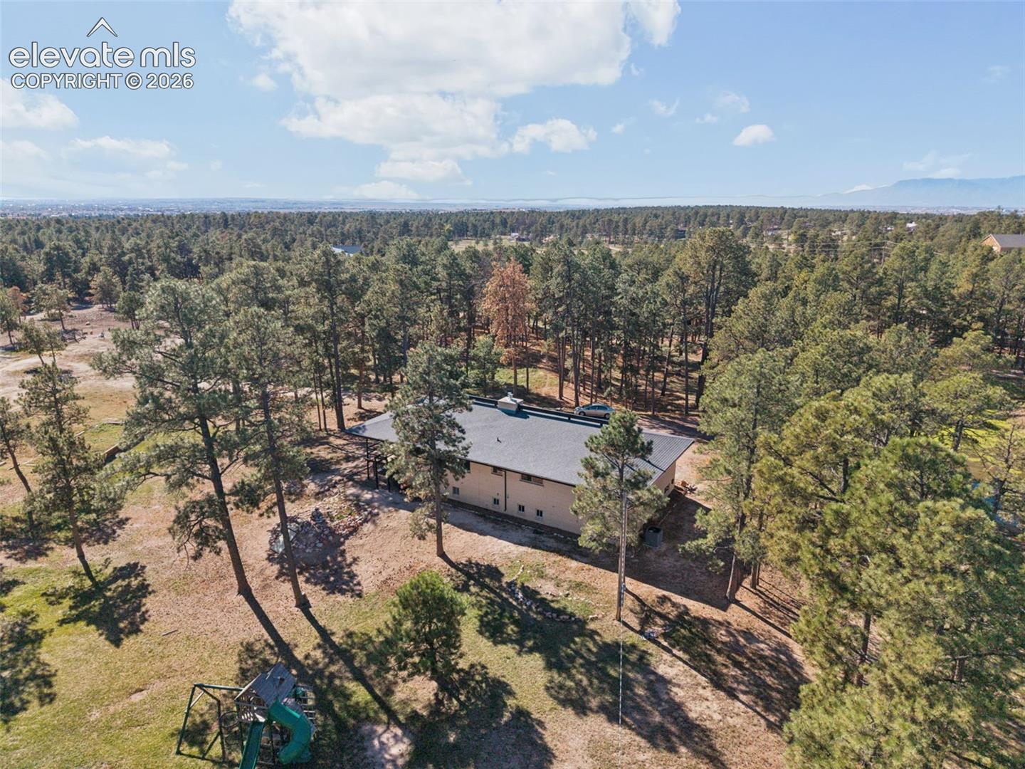 Aerial perspective of a single-story residence featuring a low-pitch roof, expansive natural lot, and mature pine tree coverage